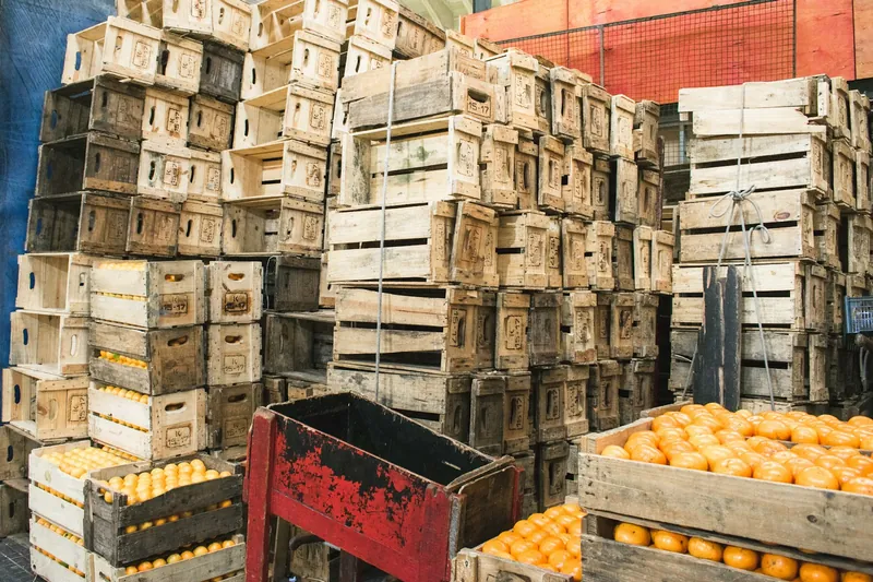 Gestapelde houten fruitkisten in een groothandelsmagazijn, vooraan kisten vol sinaasappels