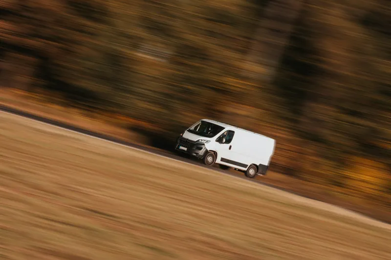 Witte bestelwagen in beweging op een weg, met een vervaagde herfstachtergrond